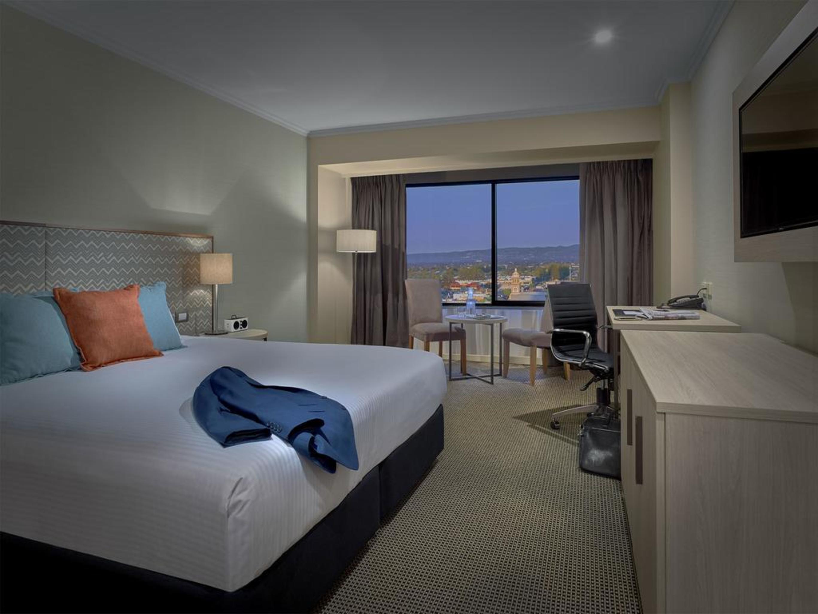 Stamford Grand Adelaide Hotel Гленелг Екстериор снимка The photo shows a modern hotel room. It features a large double bed with white bedding and decorative pillows in orange and blue. There's a nightstand with lamps on either side of the bed. A large window overlooks a view outside, and there's a desk a