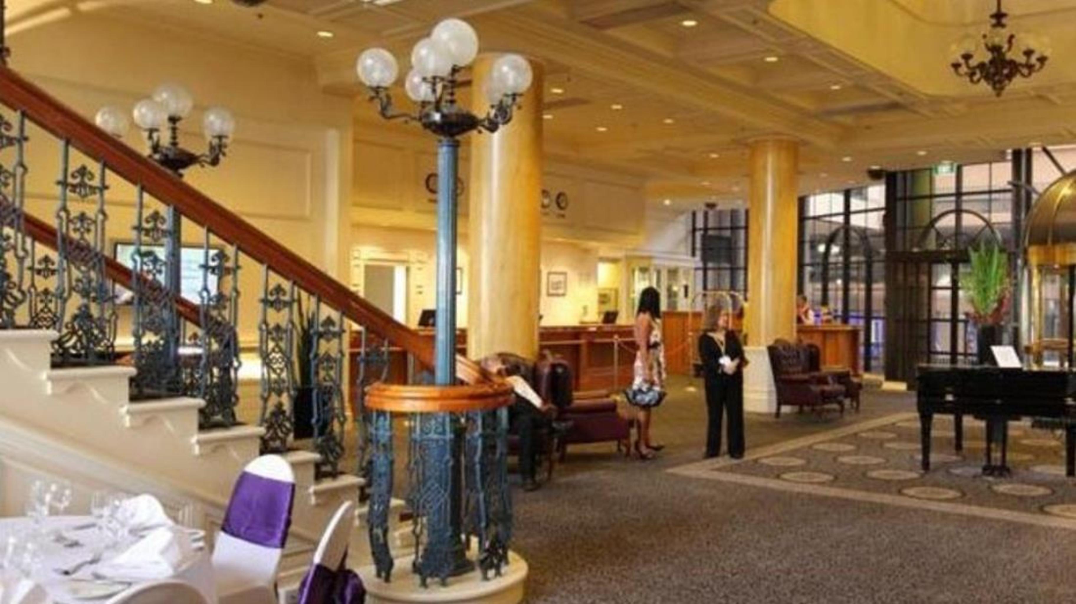 Stamford Grand Adelaide Hotel Гленелг Екстериор снимка The photo shows the interior of a hotel lobby. It features a spacious area with a high ceiling and elegant decor. There is a staircase with a decorative railing leading to an upper level. In the foreground, some guests and staff are present, and ther
