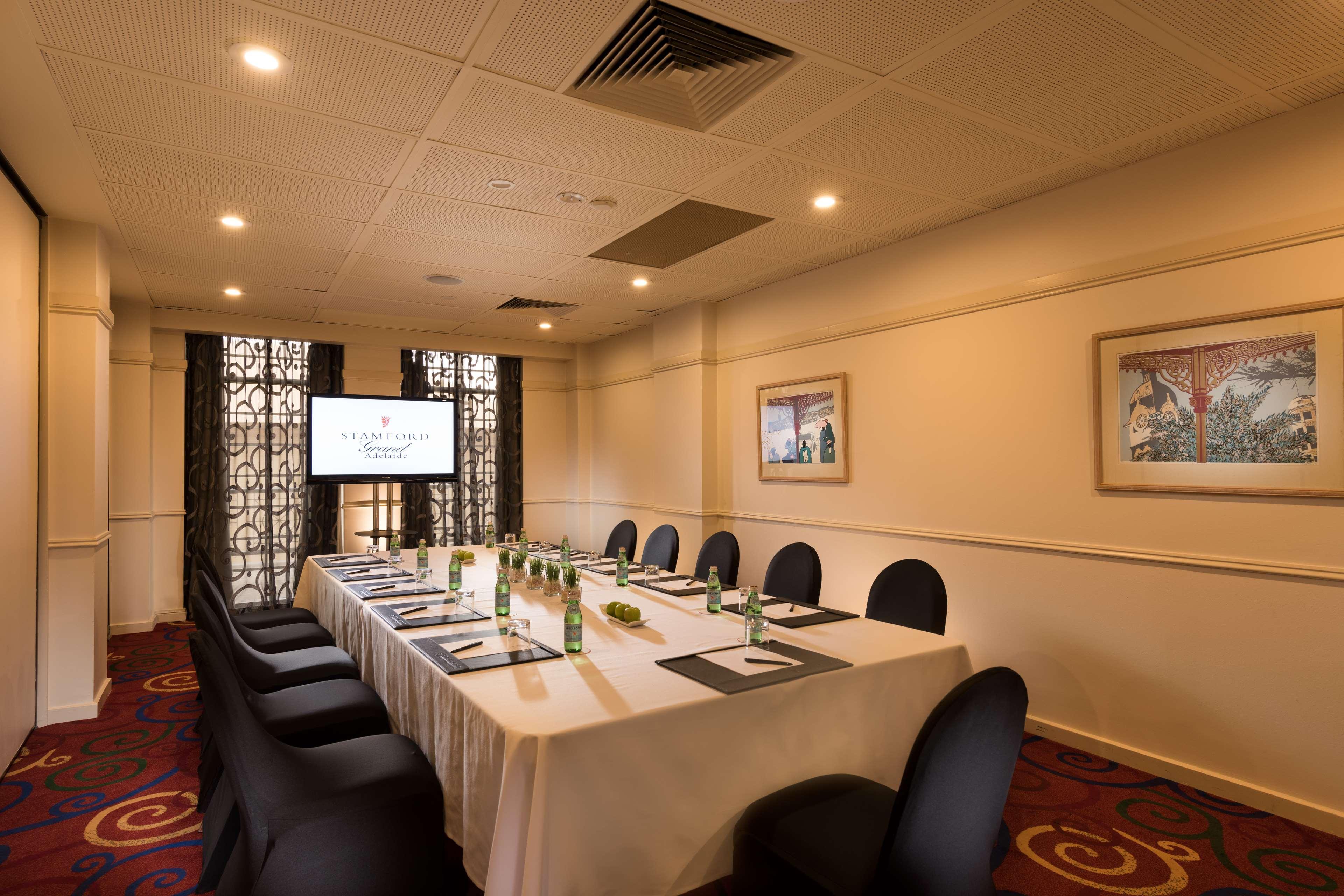 Stamford Grand Adelaide Hotel Гленелг Екстериор снимка The photo shows a conference room with a long rectangular table set for a meeting. The table is covered with a white tablecloth and has several place settings, including notebooks, pens, and water bottles. There are black chairs around the table, and