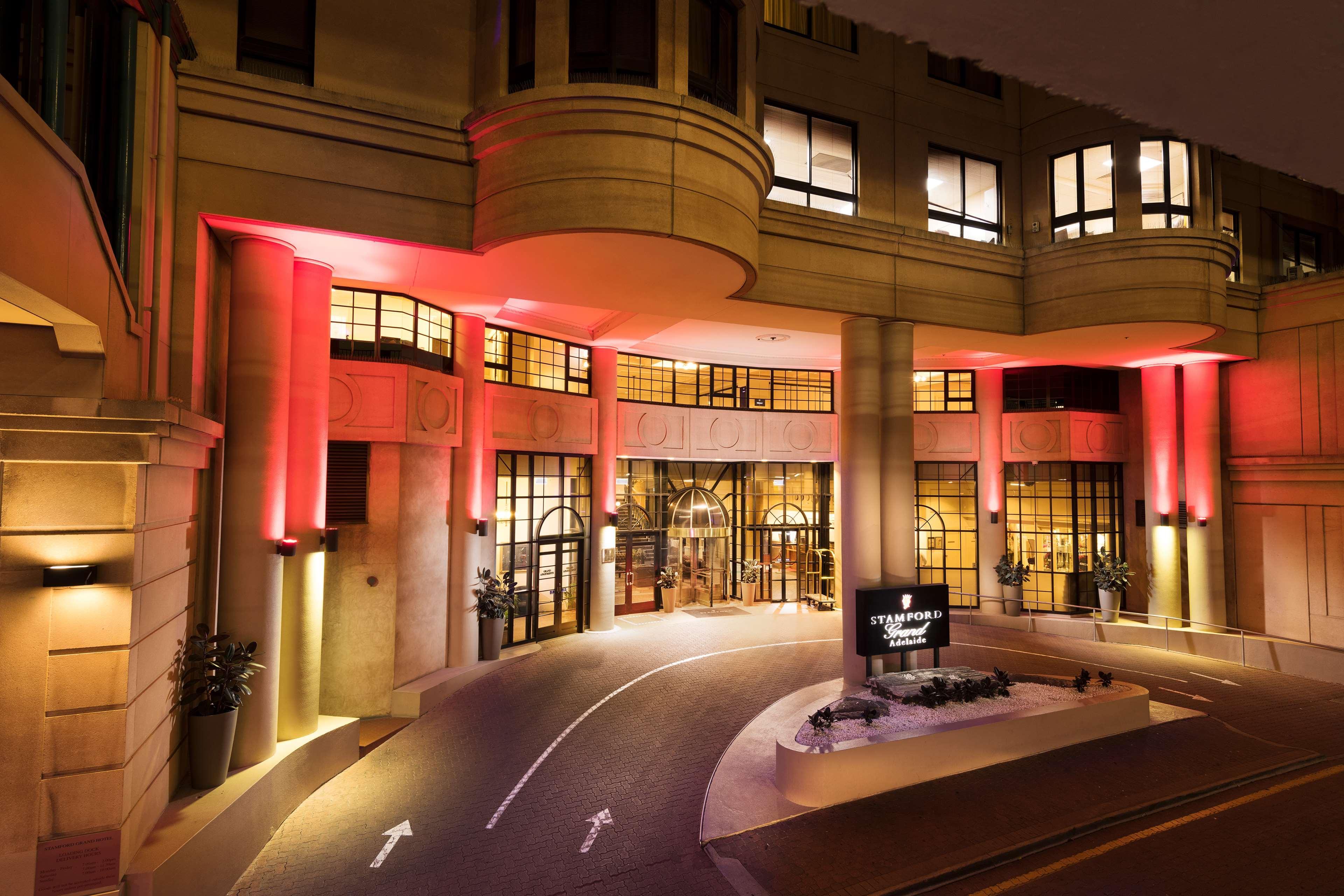 Stamford Grand Adelaide Hotel Гленелг Екстериор снимка The photo shows the entrance of a hotel or luxury building at night. The façade features a modern architectural style with large windows and an elegant entrance. The area is illuminated with red lighting, creating an inviting atmosphere. There appear