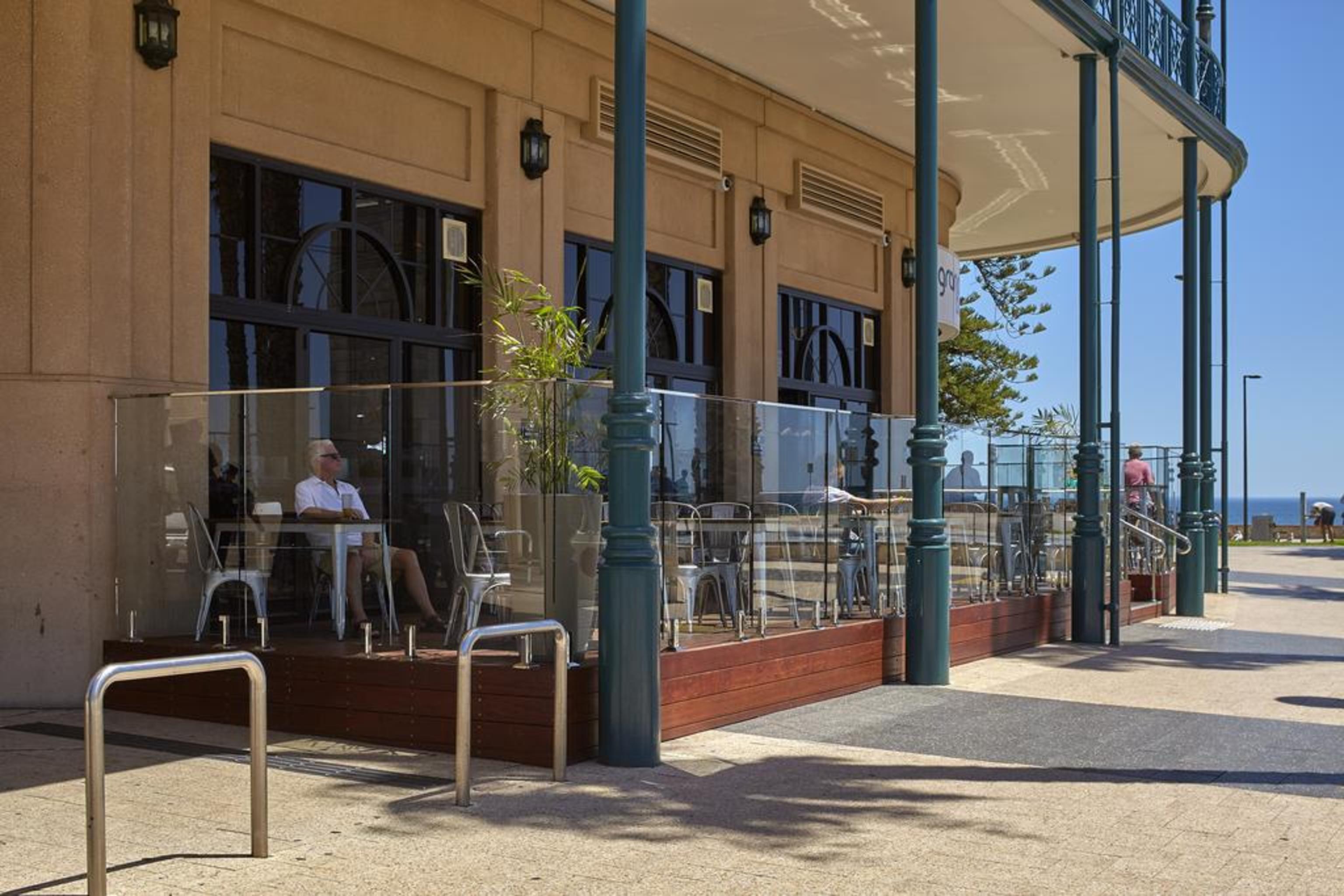 Stamford Grand Adelaide Hotel Гленелг Екстериор снимка The photo shows the exterior of a cafe or restaurant with a large outdoor seating area. There are glass barriers around the seating, providing a view of the outside while maintaining a sense of enclosure. The building has a modern architectural style