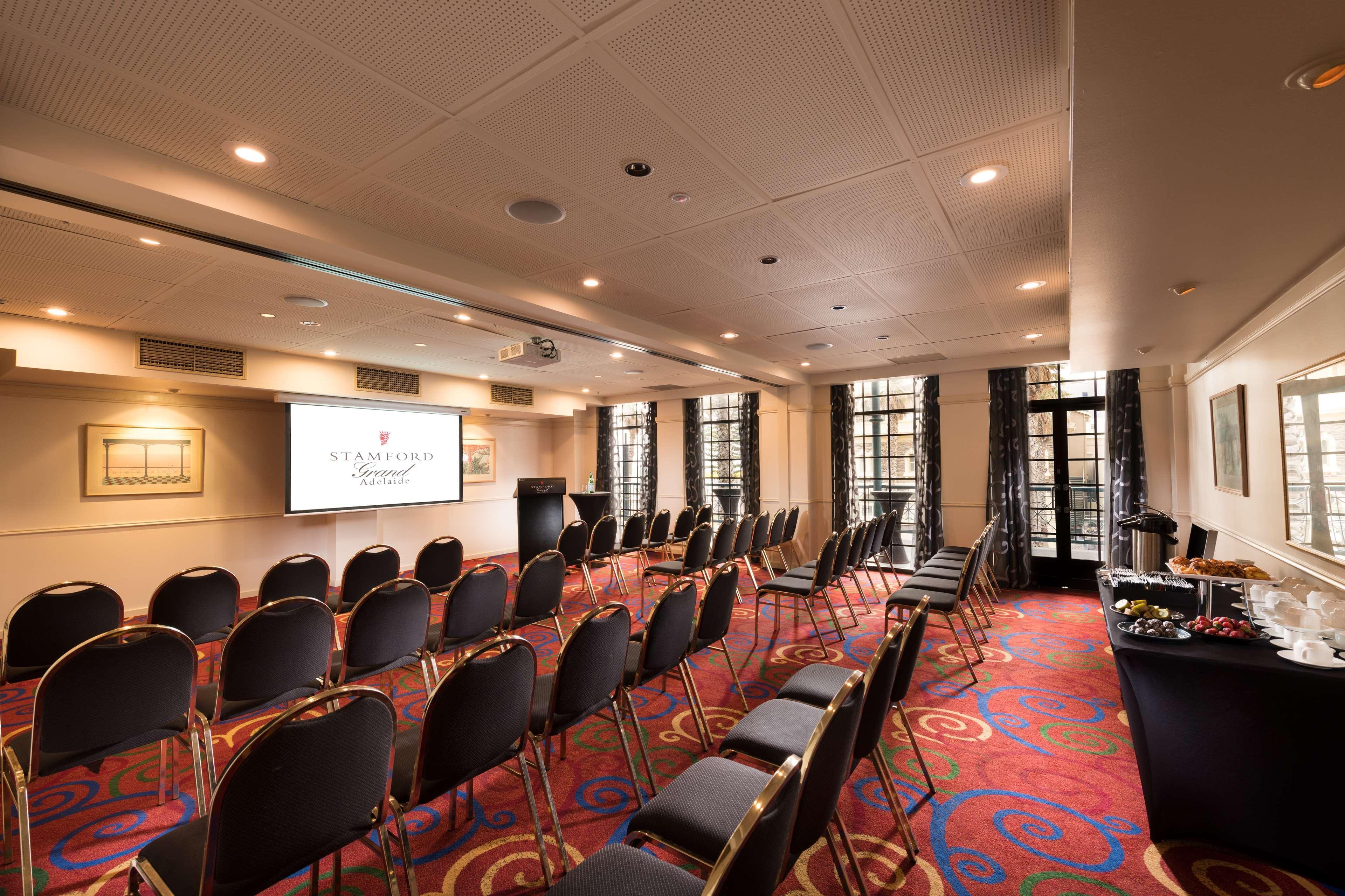 Stamford Grand Adelaide Hotel Гленелг Екстериор снимка The photo shows a conference room set up for an event. There are rows of black chairs arranged in a semicircular formation facing a presentation screen at the front. The room features large windows that allow natural light to enter, and the flooring 