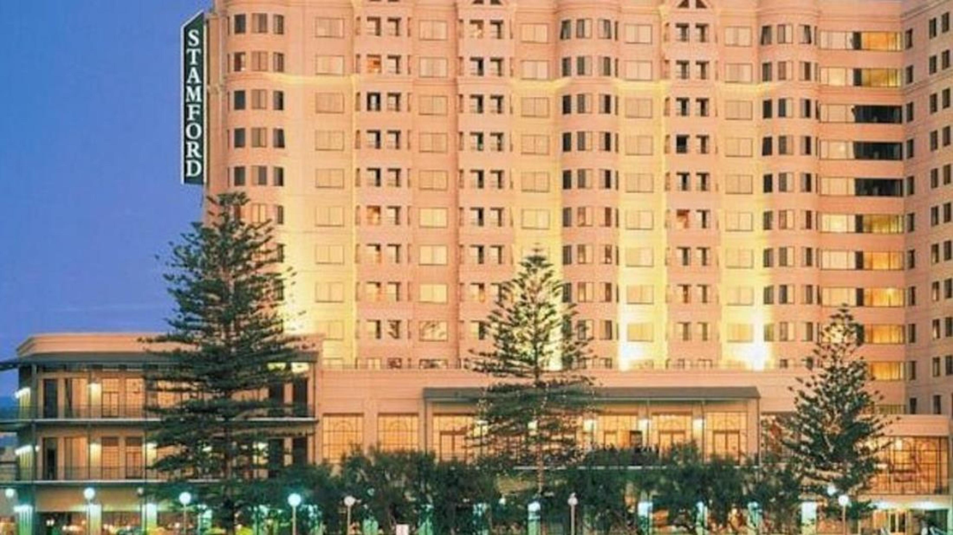 Stamford Grand Adelaide Hotel Гленелг Екстериор снимка The photo shows a tall, modern building illuminated at night, likely a hotel, with the name "Stamford" prominently displayed on its side. Surrounding the building are several palm trees and landscaped areas, suggesting a tropical or coastal location.
