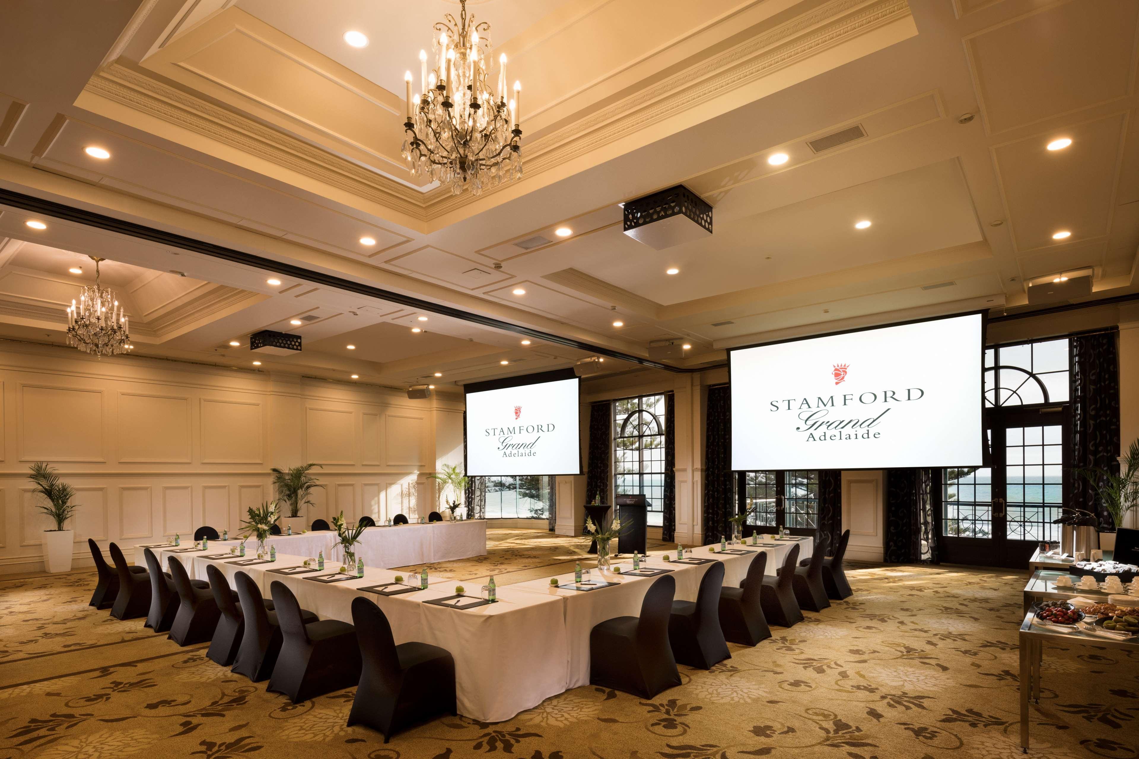Stamford Grand Adelaide Hotel Гленелг Екстериор снимка The photo shows a spacious and elegantly designed conference room. The room features a long table set for a meeting, surrounded by stylish chairs. Two large screens are positioned at the front, displaying the logo "Stamford Grand Melbourne." The ceil