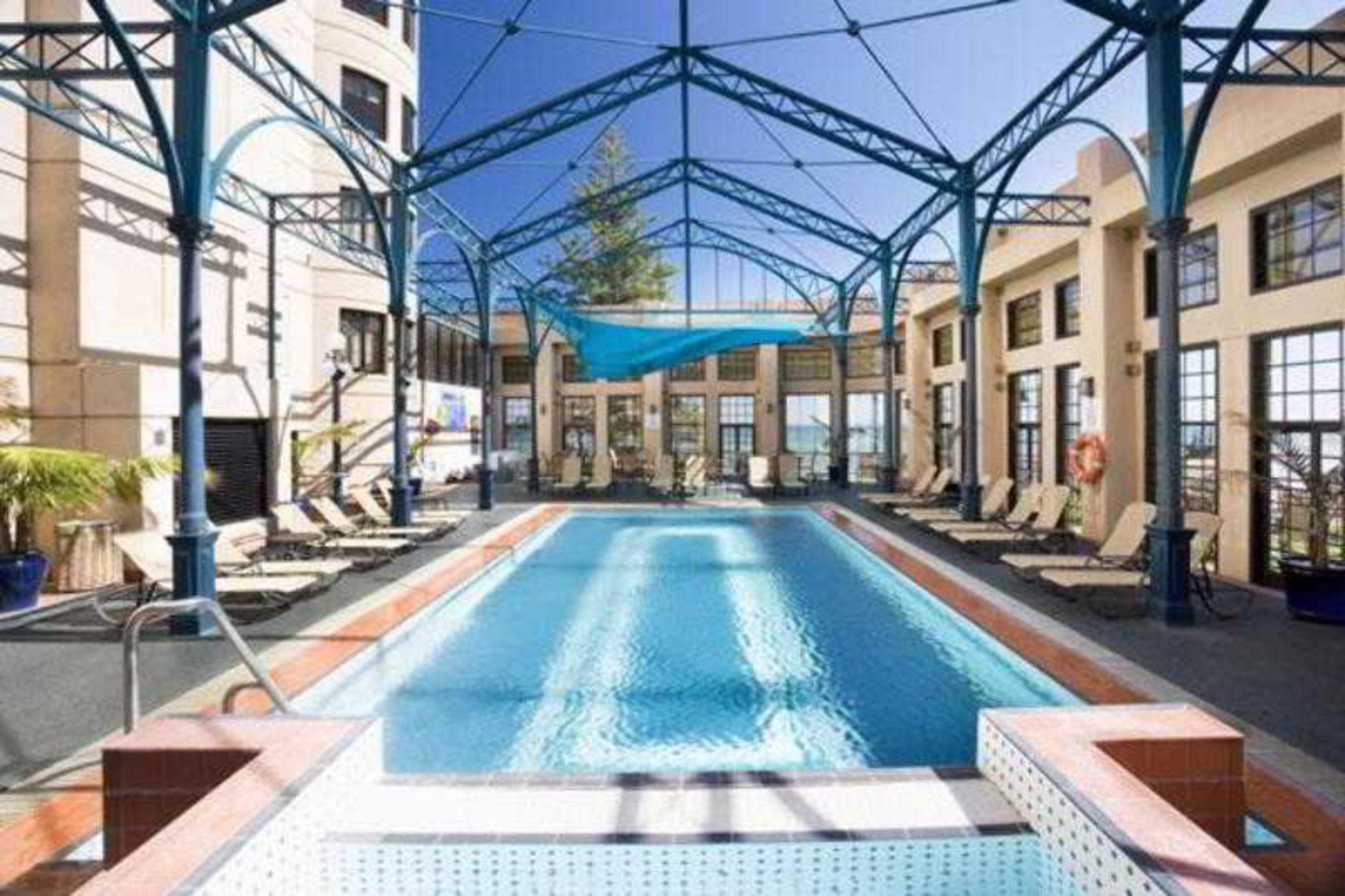 Stamford Grand Adelaide Hotel Гленелг Съоръжения снимка The photo shows an indoor swimming pool area. The pool is rectangular and features a blue cover above, supported by a metal frame. Surrounding the pool are several lounge chairs, and the space is well-lit with large windows allowing natural light to 